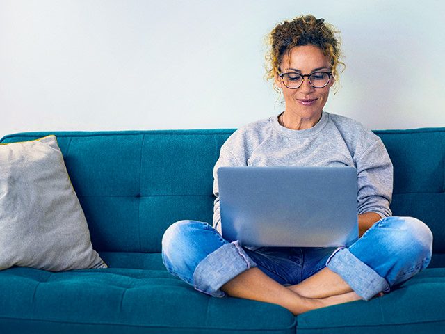 Eine Frau sitzt auf einer Couch und hat einen Laptop auf dem Schoß